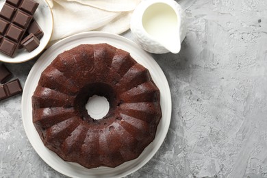 Photo of Tasty bundt cake, pieces of chocolate and milk on grey table, flat lay. Space for text