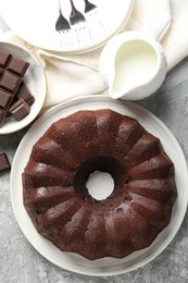 Photo of Tasty bundt cake, pieces of chocolate and milk on grey table, flat lay