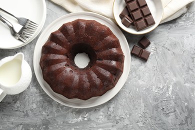 Photo of Tasty bundt cake, pieces of chocolate and milk on grey table, flat lay. Space for text