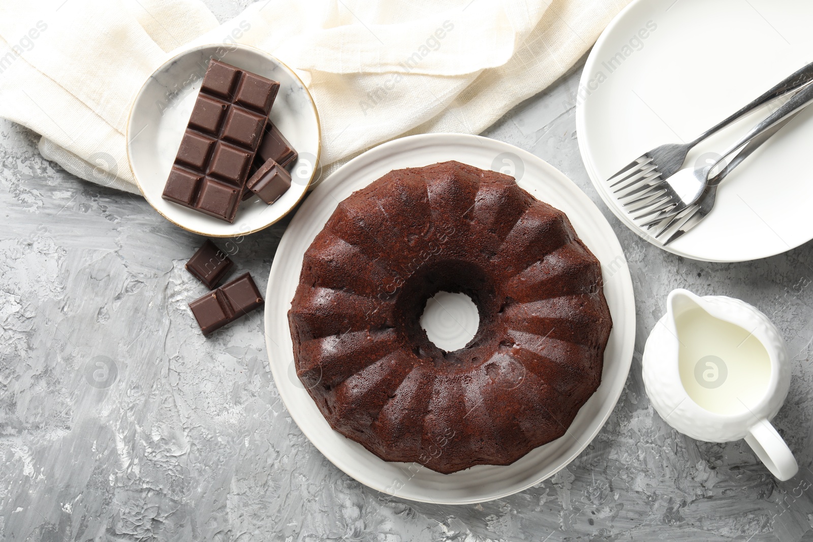 Tasty bundt cake, pieces of chocolate and milk on grey table, flat lay Photo of Tasty bundt cake, pieces of chocolate and milk on grey table, flat lay