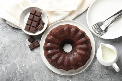 Photo of Tasty bundt cake, pieces of chocolate and milk on grey table, flat lay