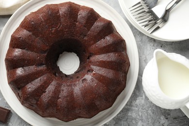 Photo of Tasty bundt cake, pieces of chocolate and milk on grey table, flat lay