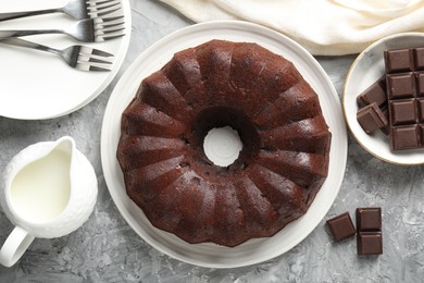 Photo of Tasty bundt cake, pieces of chocolate and milk on grey table, flat lay