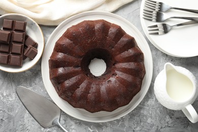 Photo of Tasty bundt cake, pieces of chocolate and milk on grey table, flat lay