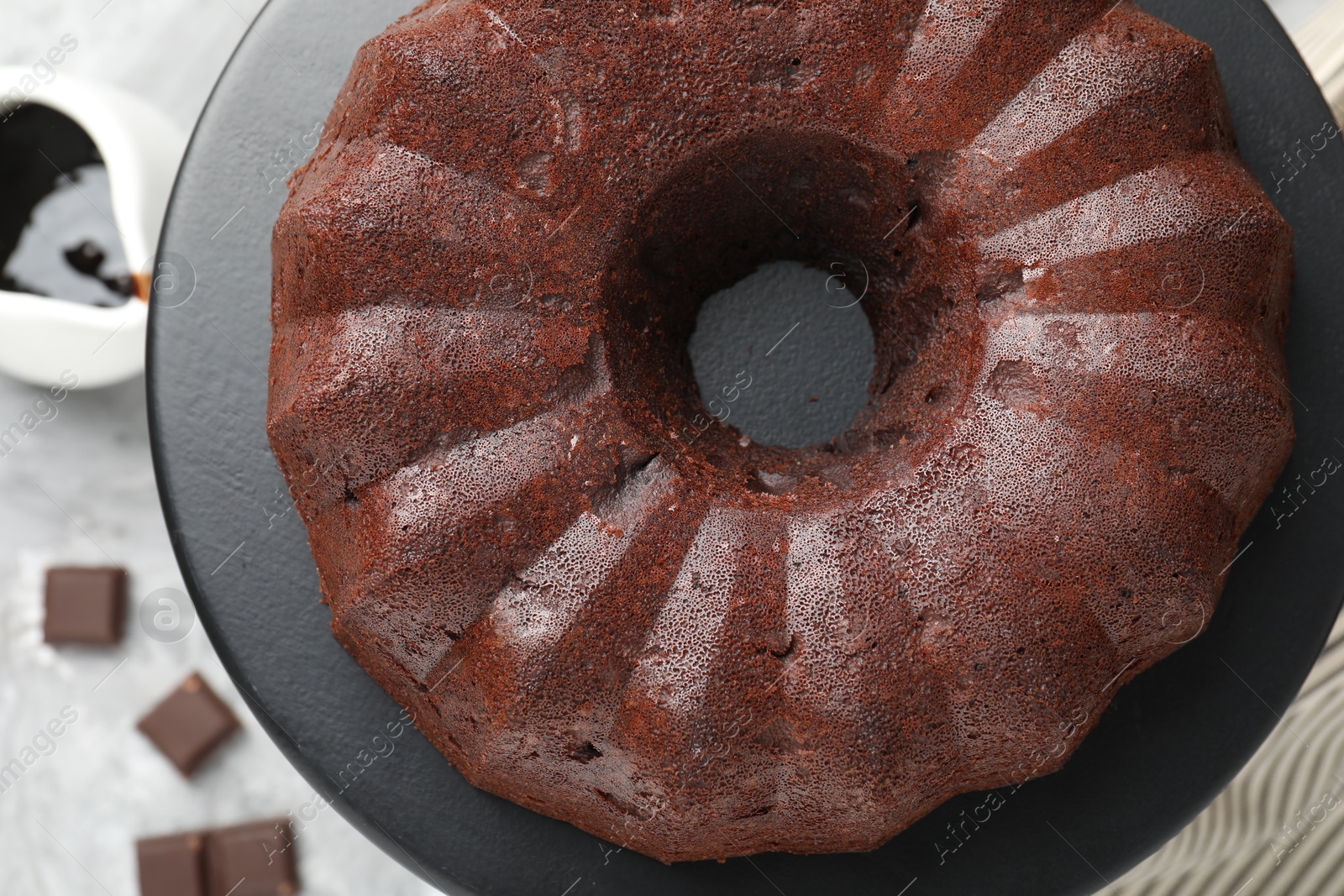 Tasty bundt cake, pieces of chocolate and sauce on table, flat lay Photo of Tasty bundt cake, pieces of chocolate and sauce on table, flat lay