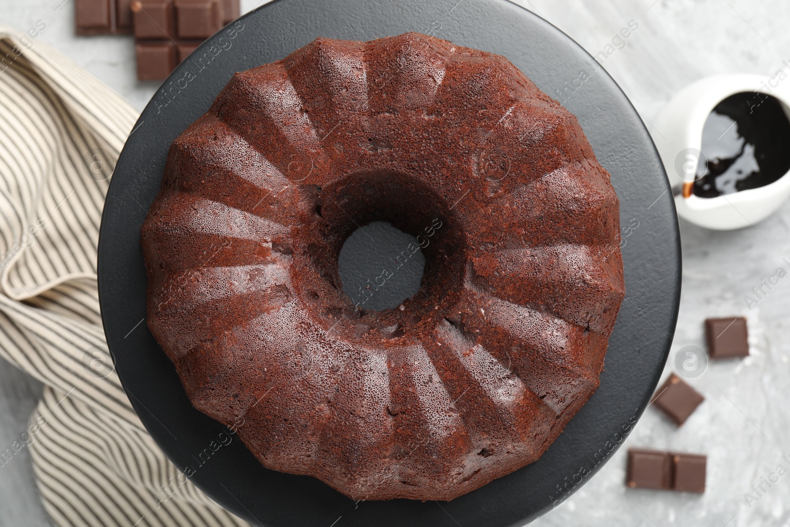 Tasty bundt cake, pieces of chocolate and sauce on grey table, flat lay Photo of Tasty bundt cake, pieces of chocolate and sauce on grey table, flat lay