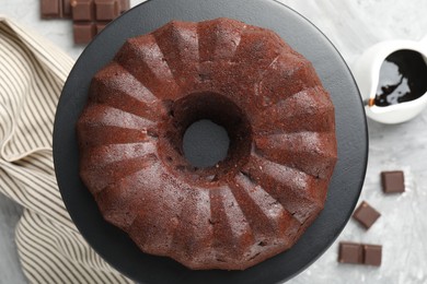 Photo of Tasty bundt cake, pieces of chocolate and sauce on grey table, flat lay