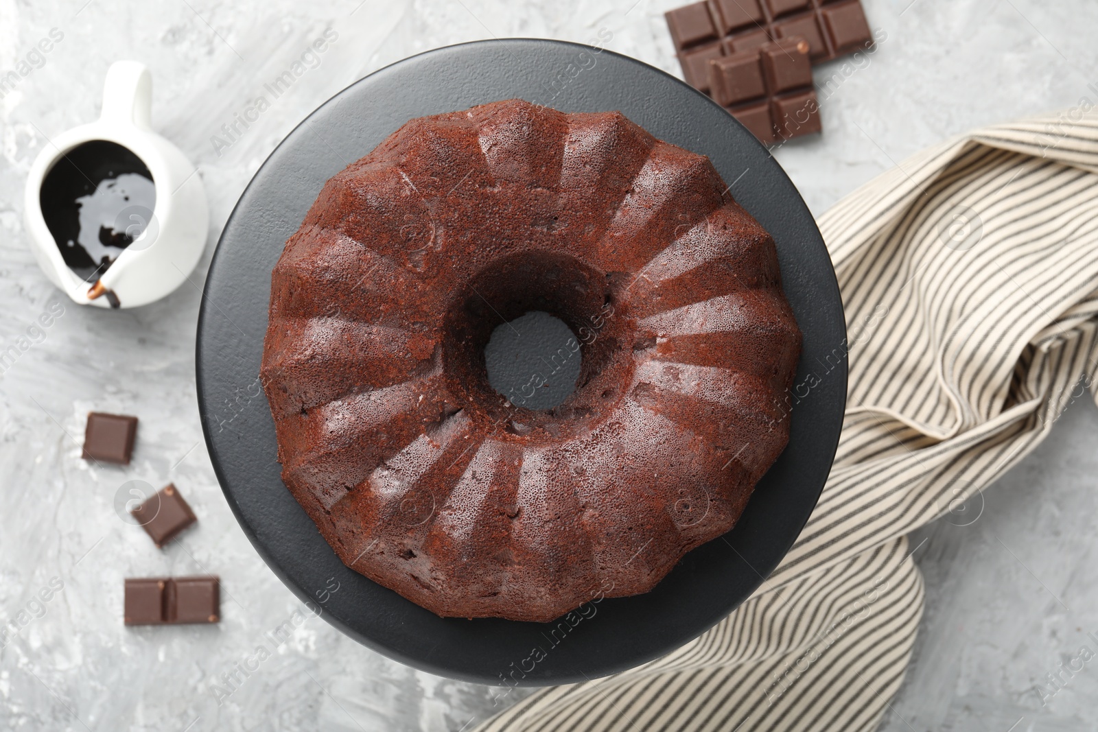 Tasty bundt cake, pieces of chocolate and sauce on grey table, flat lay Photo of Tasty bundt cake, pieces of chocolate and sauce on grey table, flat lay
