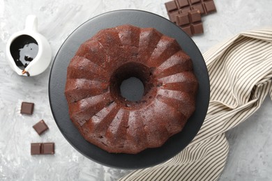 Photo of Tasty bundt cake, pieces of chocolate and sauce on grey table, flat lay