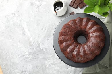 Photo of Tasty bundt cake, pieces of chocolate, sauce and green leaves on grey table, flat lay. Space for text