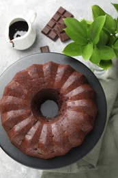 Photo of Tasty bundt cake, pieces of chocolate, sauce and green leaves on grey table, flat lay