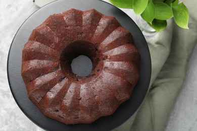 Photo of Tasty chocolate bundt cake and green leaves on table, flat lay