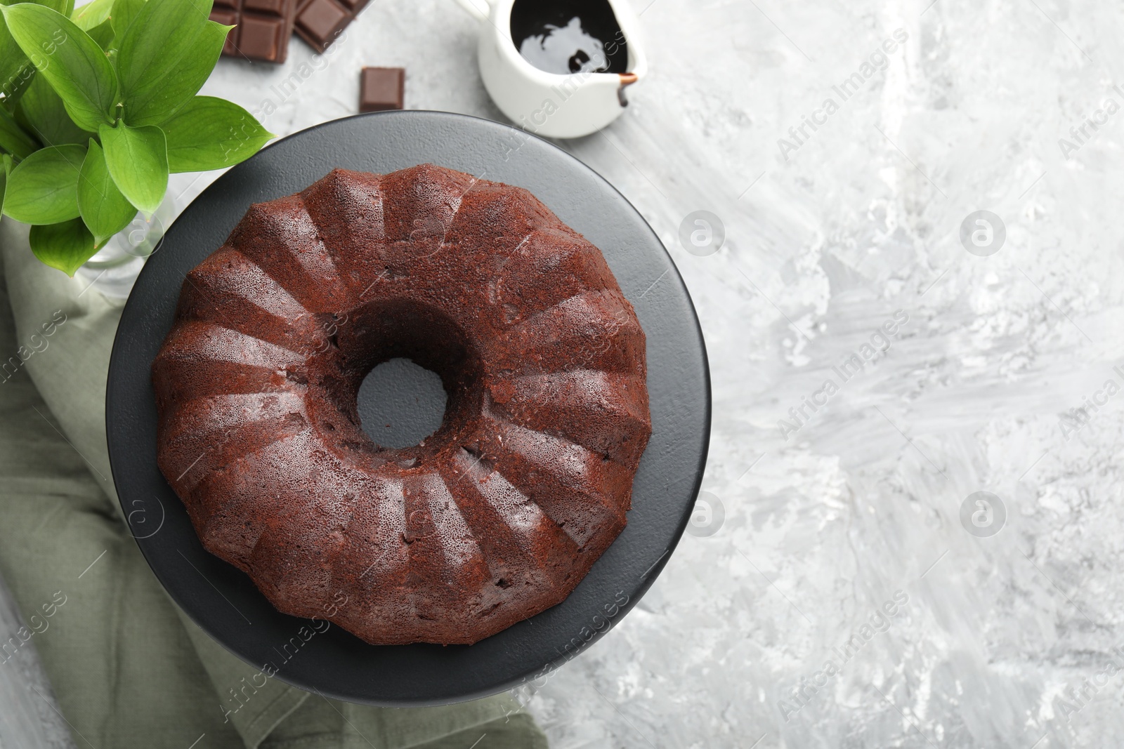 Tasty bundt cake, pieces of chocolate, sauce and green leaves on grey table, flat lay. Space for text Photo of Tasty bundt cake, pieces of chocolate, sauce and green leaves on grey table, flat lay. Space for text