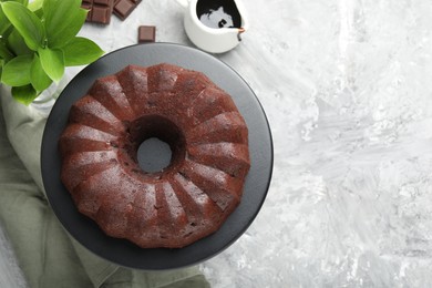 Photo of Tasty bundt cake, pieces of chocolate, sauce and green leaves on grey table, flat lay. Space for text