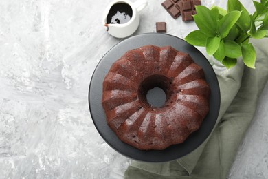 Photo of Tasty bundt cake, pieces of chocolate, sauce and green leaves on grey table, flat lay. Space for text