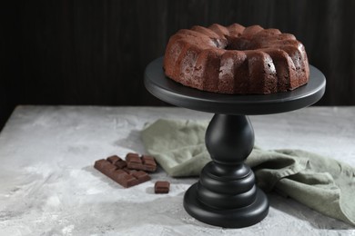 Photo of Tasty bundt cake and pieces of chocolate on grey table, closeup. Space for text