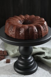 Photo of Tasty bundt cake and pieces of chocolate on grey table, closeup