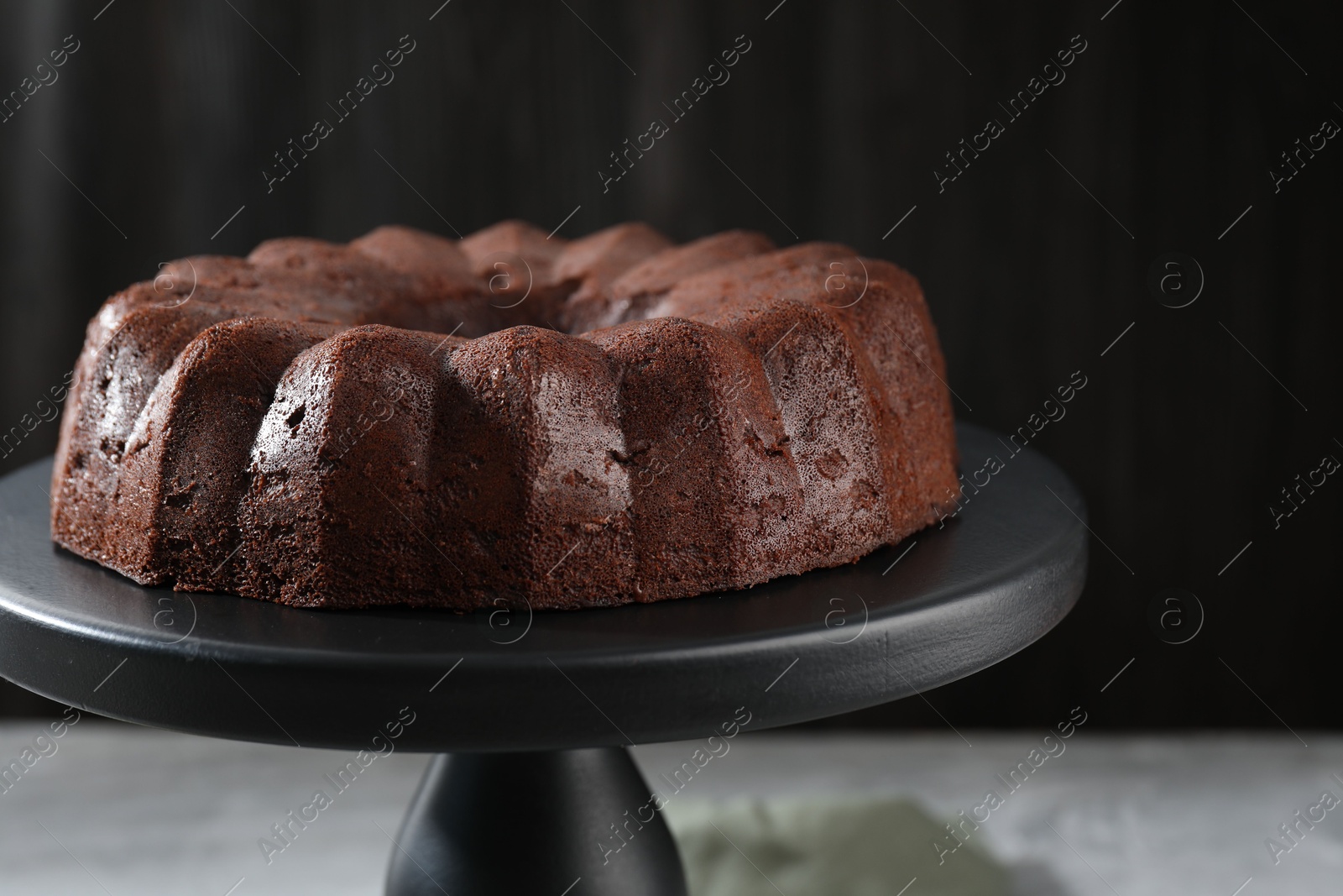 Tasty chocolate bundt cake on stand against blurred background, closeup Photo of Tasty chocolate bundt cake on stand against blurred background, closeup