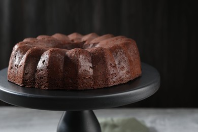 Photo of Tasty chocolate bundt cake on stand against blurred background, closeup
