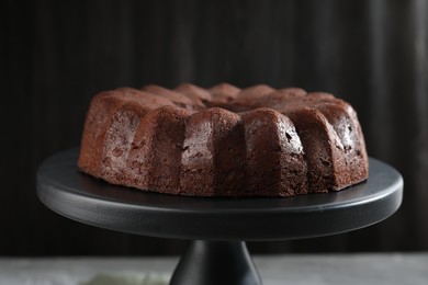 Photo of Tasty chocolate bundt cake on stand against blurred background, closeup