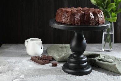 Photo of Tasty bundt cake, pieces of chocolate, sauce and green leaves on grey table
