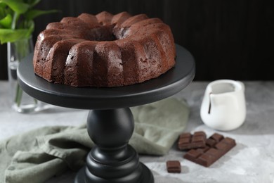Photo of Tasty bundt cake, pieces of chocolate, sauce and green leaves on grey table, closeup