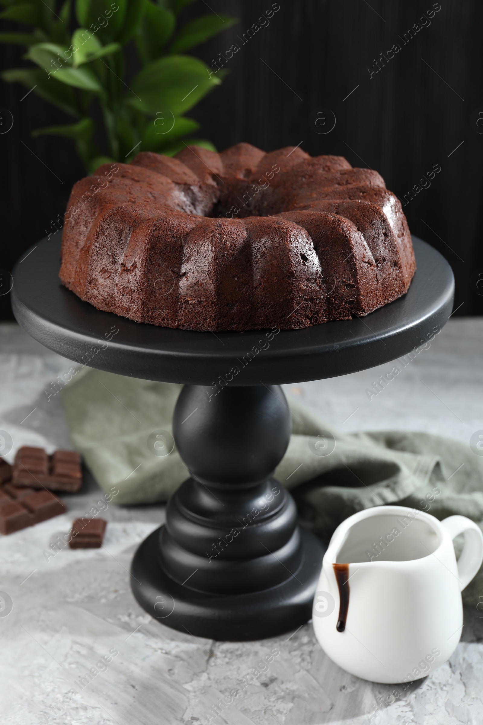 Tasty bundt cake, pieces of chocolate, sauce and green leaves on grey table, closeup Photo of Tasty bundt cake, pieces of chocolate, sauce and green leaves on grey table, closeup