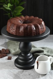 Photo of Tasty bundt cake, pieces of chocolate, sauce and green leaves on grey table, closeup