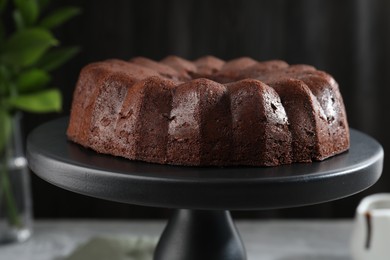 Photo of Tasty chocolate bundt cake on stand against blurred background, closeup