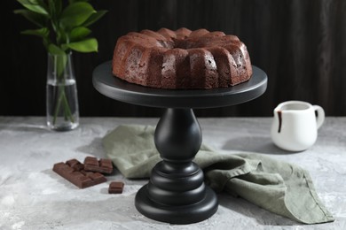 Photo of Tasty bundt cake, pieces of chocolate, sauce and green leaves on grey table, closeup