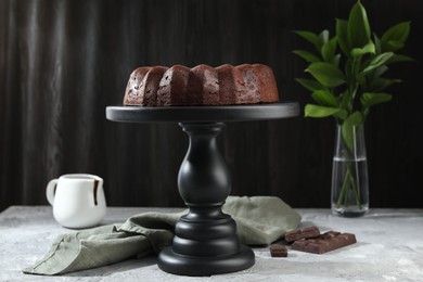 Photo of Tasty bundt cake, pieces of chocolate, sauce and green leaves on grey table