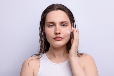 Photo of Beautiful woman applying skincare product onto her face on light grey background, closeup