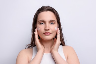 Photo of Beautiful woman applying skincare product onto her face on light grey background, closeup