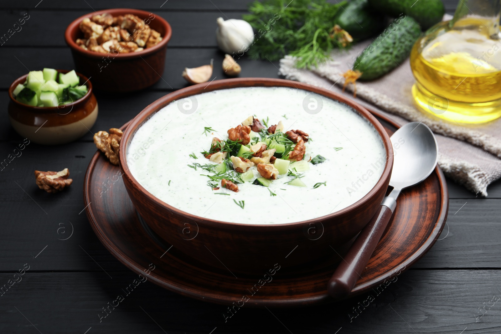 Photo of Tasty cucumber soup with dill and walnuts served on black wooden table, closeup