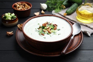 Photo of Tasty cucumber soup with dill and walnuts served on black wooden table, closeup