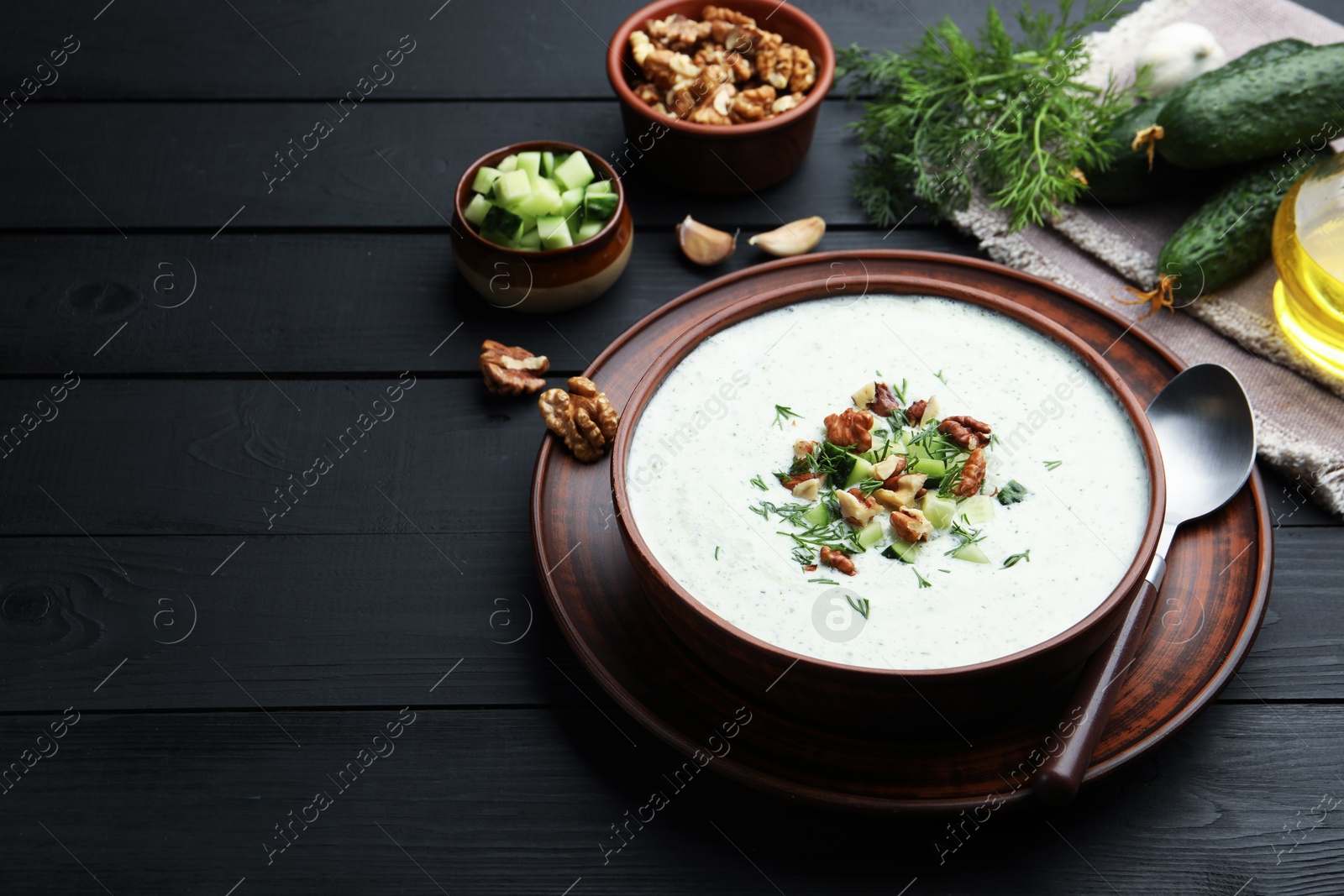 Photo of Tasty cucumber soup with dill and walnuts served on black wooden table. Space for text