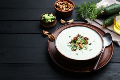 Photo of Tasty cucumber soup with dill and walnuts served on black wooden table. Space for text