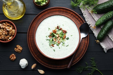 Photo of Tasty cucumber soup with dill and walnuts served on black wooden table, flat lay