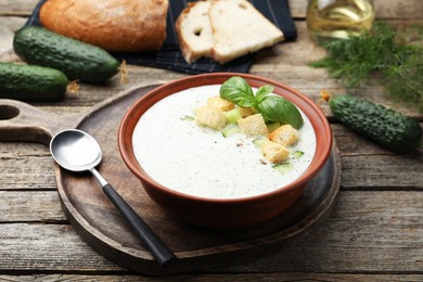Photo of Tasty cucumber soup with croutons and basil served on wooden table, closeup