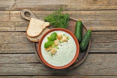 Photo of Tasty cucumber soup with croutons, basil, bread and vegetables on wooden table, flat lay
