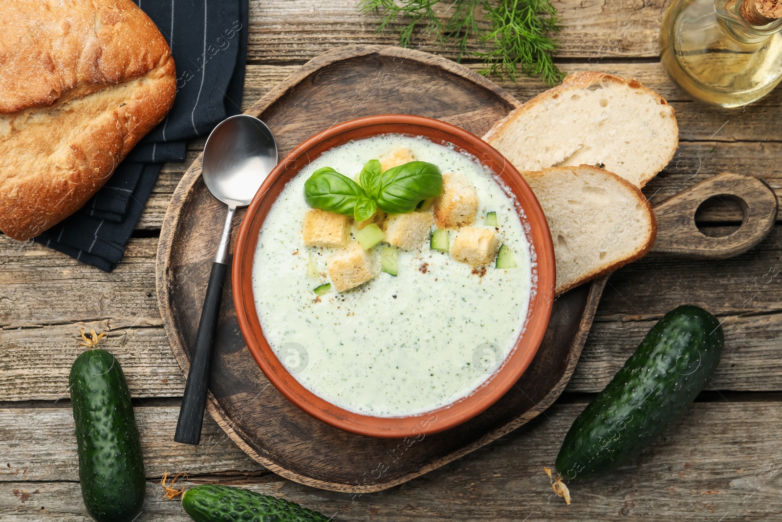 Photo of Tasty cucumber soup with croutons and basil served on wooden table, flat lay
