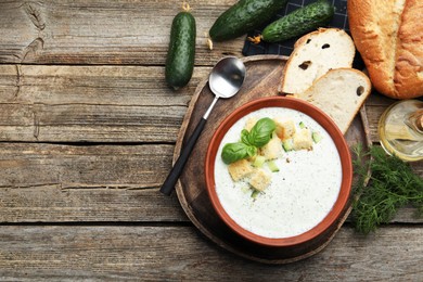 Photo of Tasty cucumber soup with croutons and basil served on wooden table, flat lay. Space for text