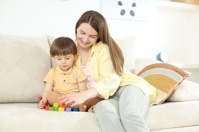 Photo of Mother and son playing with colorful cubes on sofa at home