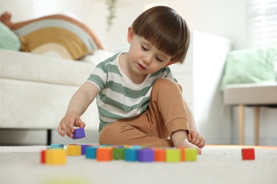 Photo of Cute little child playing with colorful cubes at home