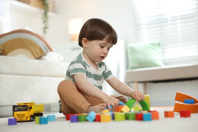 Photo of Cute little child playing with colorful cubes at home