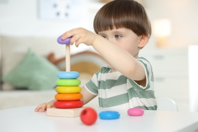 Photo of Cute little child playing with toy pyramid at table indoors