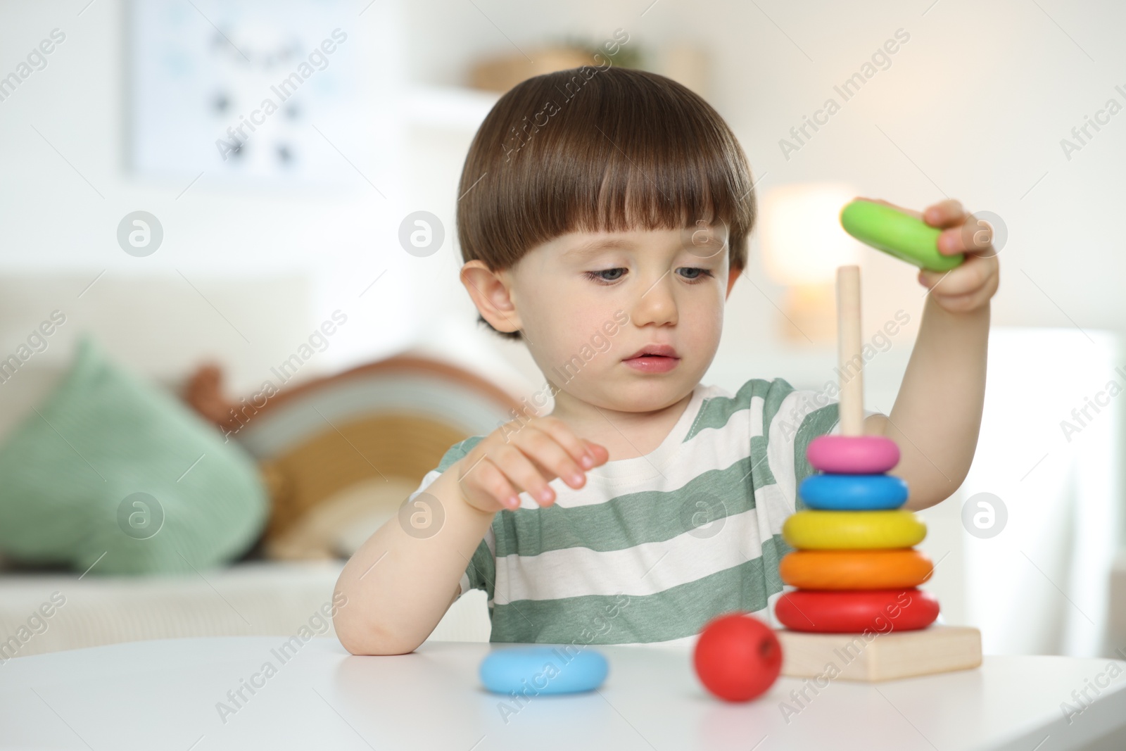 Cute little child playing with toy pyramid at table indoors Photo of Cute little child playing with toy pyramid at table indoors