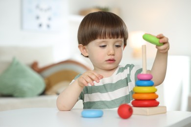 Photo of Cute little child playing with toy pyramid at table indoors