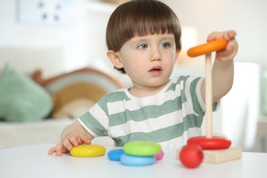 Photo of Cute little child playing with toy pyramid at table indoors