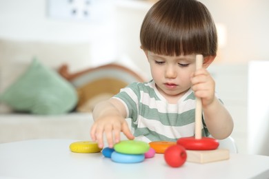 Photo of Cute little child playing with toy pyramid at table indoors